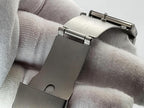 Close-up of a stainless steel Aokulasic Open Heart Automatic watch strap buckle and clasp held by a white textured glove.