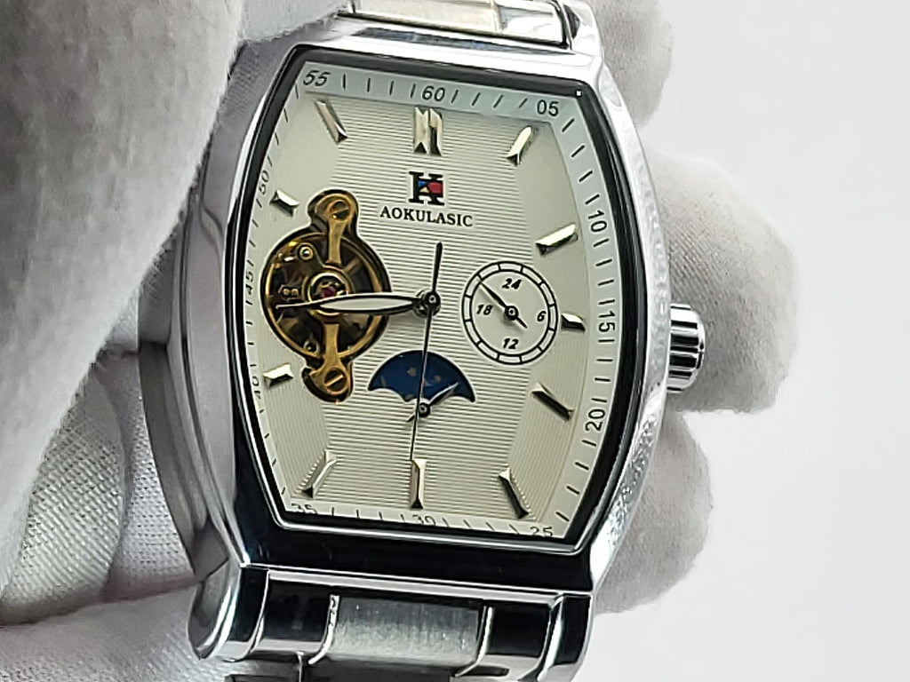 A silver stainless steel Aokulasic Open Heart Automatic wristwatch with a moonphase dial and skeletonized dial, held by a white gloved hand against a white background. The brand name 'AOKULASIC' is visible on the dial.