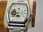 A silver stainless steel Aokulasic Open Heart Automatic wristwatch with a white dial, featuring an open-heart window showing gold-toned gears, a moon phase indicator, and a date window. The watch is displayed on a beige cushion mounted on a wooden stand against a neutral background.