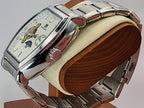 A silver-tone Aokulasic Open Heart Automatic stainless steel wristwatch with a white dial and skeletonized movement, displayed on a wooden stand with a cream cushion.
