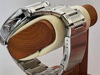 Close-up of a silver stainless steel Aokulasic Open Heart Automatic watch bracelet mounted on a wooden display stand with a cream foam insert, showing the clasp and link details.