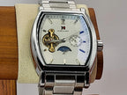 Aokulasic Open Heart Automatic men's automatic watch with a silver stainless steel case and link bracelet, featuring a white dial with skeletonized details, blue hands, and a moon phase indicator, displayed on a wooden stand.