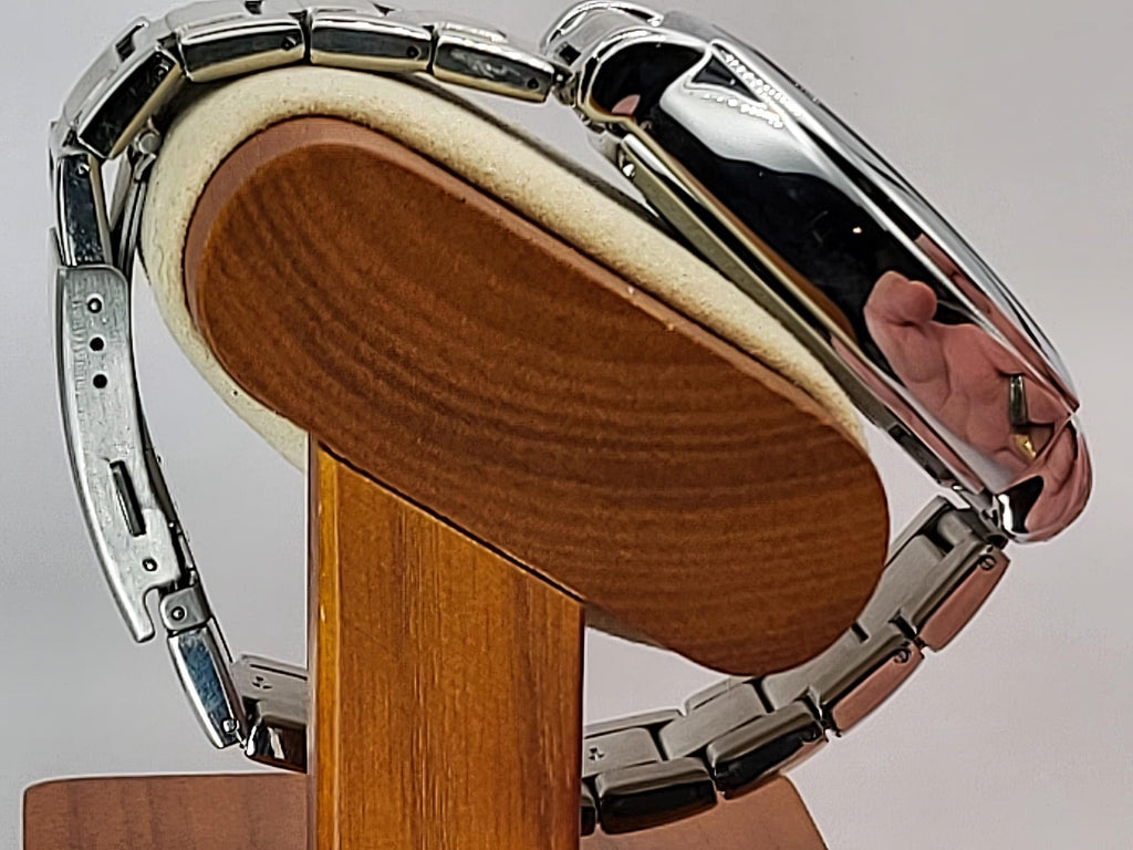 A close-up of a silver stainless steel Aokulasic Open Heart Automatic watch band with a polished chrome finish, mounted on a wooden display stand with a cream-colored foam insert.