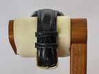 A Benrus wristwatch black embossed leather watch strap with a gold buckle, displayed on a cream-colored foam roll mounted on a wooden stand against a light gray background.