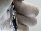A close-up side view of a silver Benrus wristwatch held by a hand wearing a white fabric glove, showing the side profile of the case and crown.