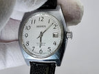 A vintage Benrus wristwatch with a silver-toned metal case, white dial, and black leather strap, held by a white gloved hand against a light gray background.