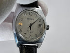 A vintage Benrus watch with a silver-toned metal case, a cream-colored dial, and a black leather strap, held by a white gloved hand against a light gray background.