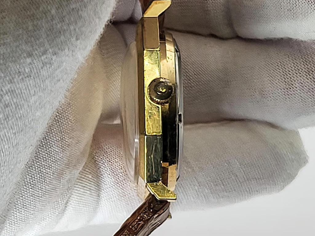 A close-up side view of a gold-toned wristwatch held against a white textured fabric background.