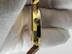 A close-up side view of a gold-toned wristwatch held against a white textured fabric background.