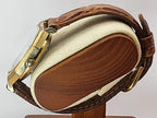 A close-up of a vintage Caravelle Day-Date watch with a brown leather strap and gold-toned case, displayed on a wooden stand against a light gray background.