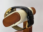 A vintage Caravelle Dual Day watch with a black leather strap and gold-toned case, displayed on a wooden stand with a cream-colored felt cushion against a light gray background.