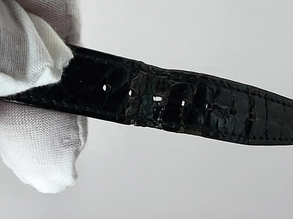 A close-up of a black embossed Léonard Genève watch strap held by a white gloved hand against a plain light gray background.