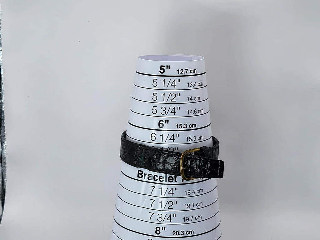A black textured leather bracelet with a gold-tone buckle for a Léonard Genève wristwatch displayed on a white plastic cone measuring chart for bracelet sizes, set against a plain light gray background.