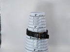 A black textured leather bracelet with a gold-tone buckle for a Léonard Genève wristwatch displayed on a white plastic cone measuring chart for bracelet sizes, set against a plain light gray background.