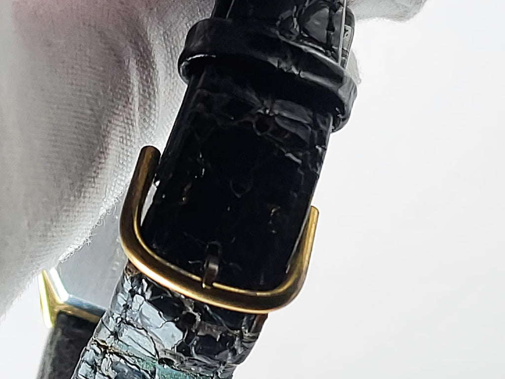 Close-up of a black embossed Léonard Genève leather watch strap with a gold-tone buckle, held against a white background.