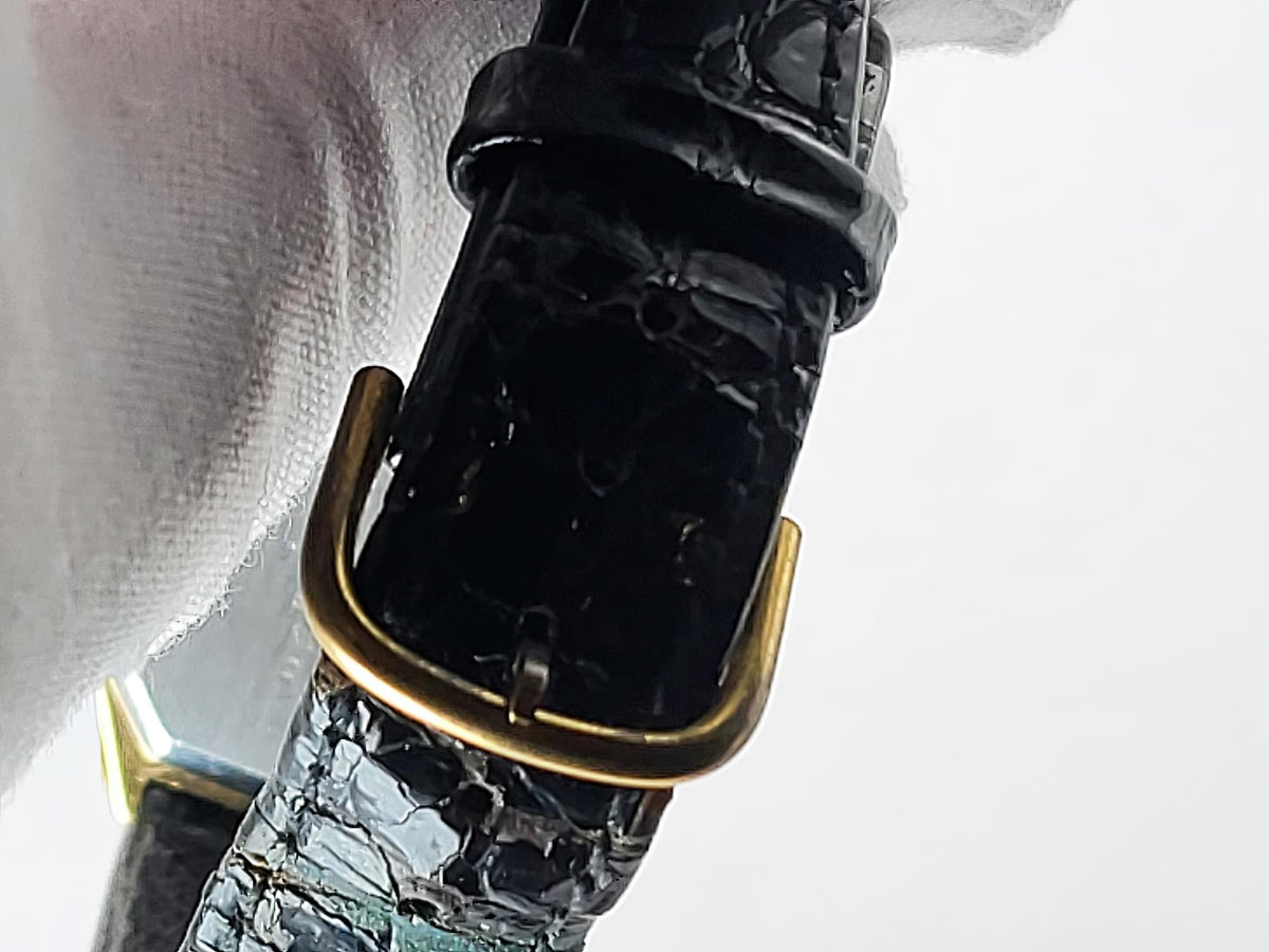 Close-up of a black embossed Léonard Genève leather watch strap with a gold-tone buckle, held against a white background.