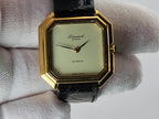A vintage Léonard Genève quartz watch with an octagonal gold-tone case, cream-colored dial, and black leather strap, held by a white gloved hand.