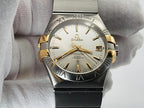 Omega Constellation wristwatch with a two-tone stainless steel and gold-tone case, featuring a white dial and Roman numeral hour markers, held in a white textured glove.