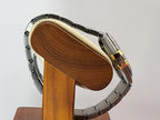 A silver-toned metal link Omega Constellation watch band with a gold-toned clasp, displayed on a wooden stand against a light gray background.