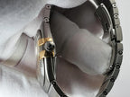Close-up of a silver-toned metal watch bracelet with a gold accent band section, for a Omega Constellation wristwatch, resting on textured fabric gloved fingers.