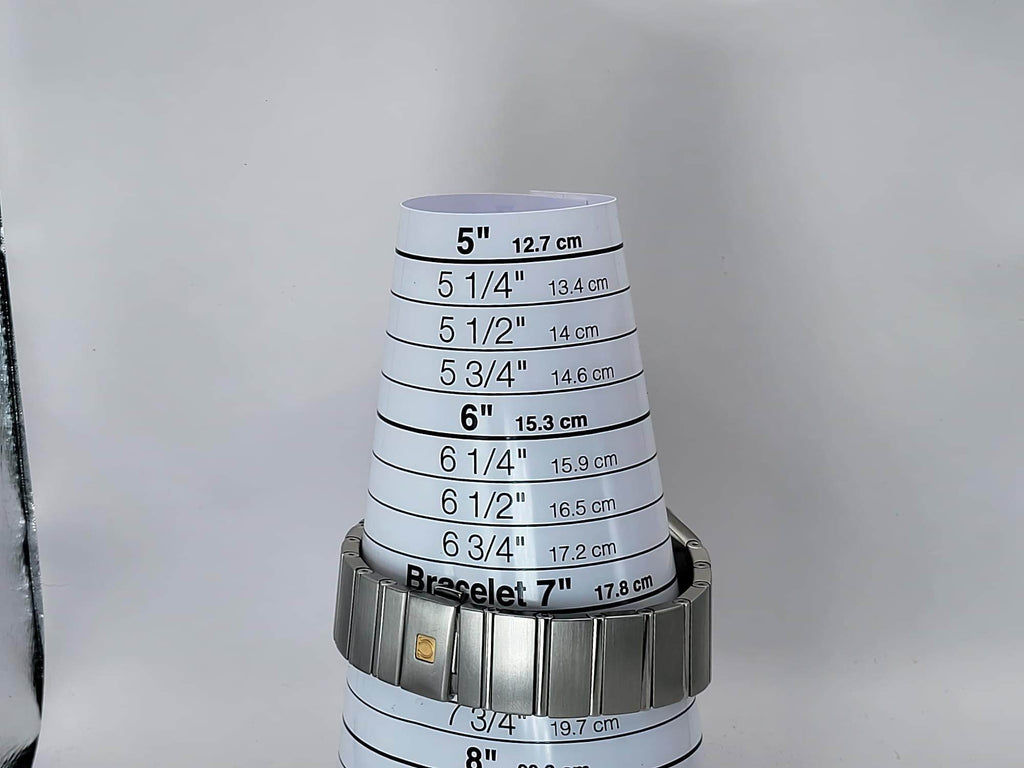 A silver metal bracelet watch wristband for a Omega Constellation watch, shown wrapped around a white cone-shaped size gauge printed with bracelet measurements in inches and centimeters.