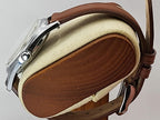 A close-up of a Reliance wristwatch with a brown leather strap and silver-toned metal case, resting on a round wooden display stand with a cream felt lining.