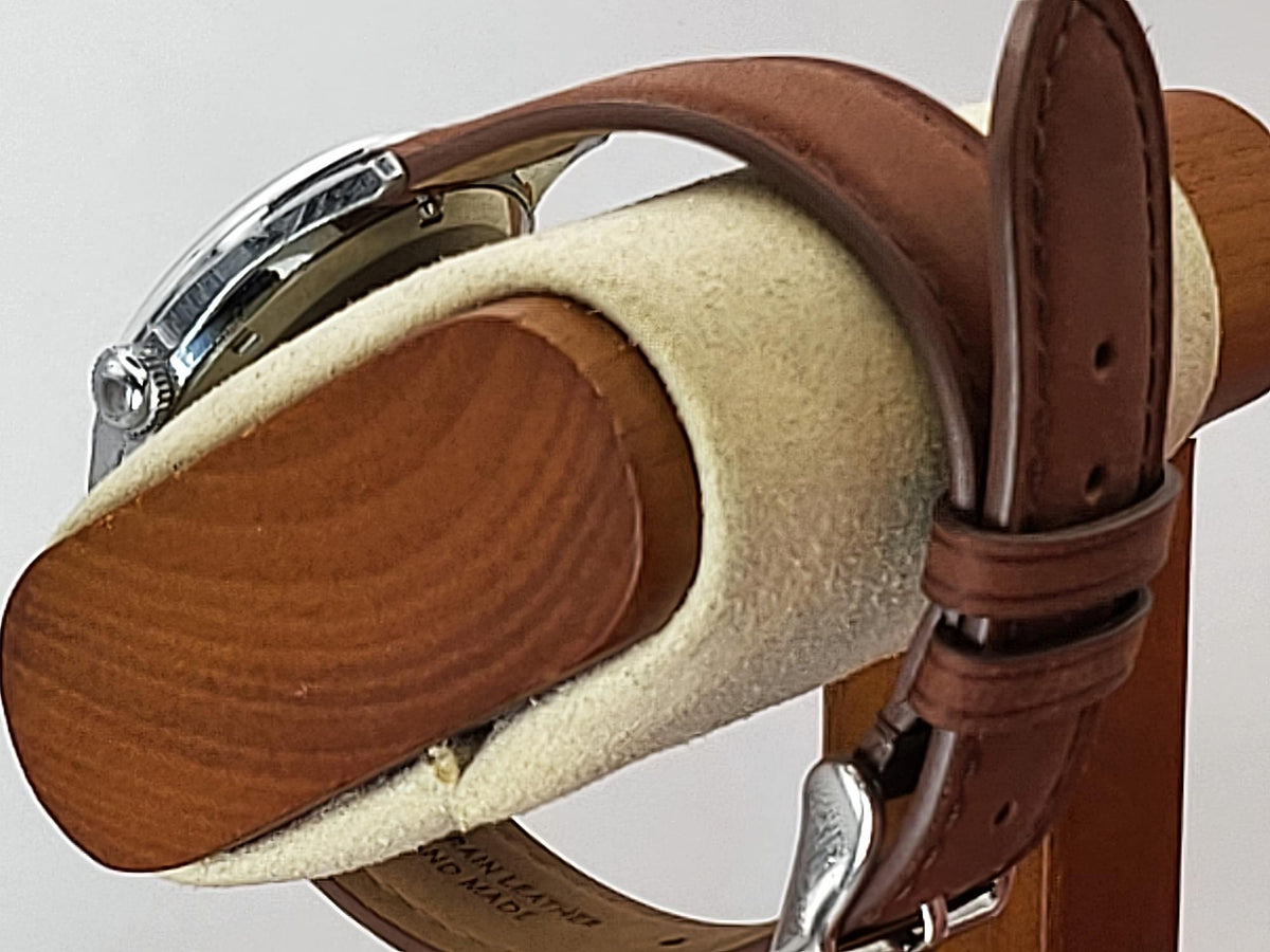 A close-up of a brown leather watch strap for a Reliance wristwatch mounted on a wooden and felt display stand, with part of a silver-toned watch case visible.