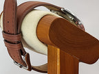 A close-up of a brown leather watch strap with a silver buckle for a Reliance wristwatch, draped over a wooden and cream-colored watch display stand.