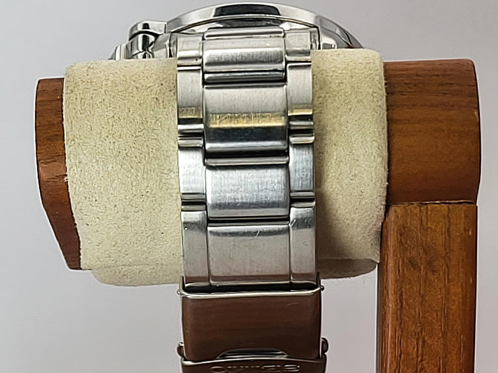 Close-up of a stainless steel Seiko Flightmaster watch band mounted on a wooden display stand with a beige velvet roll.