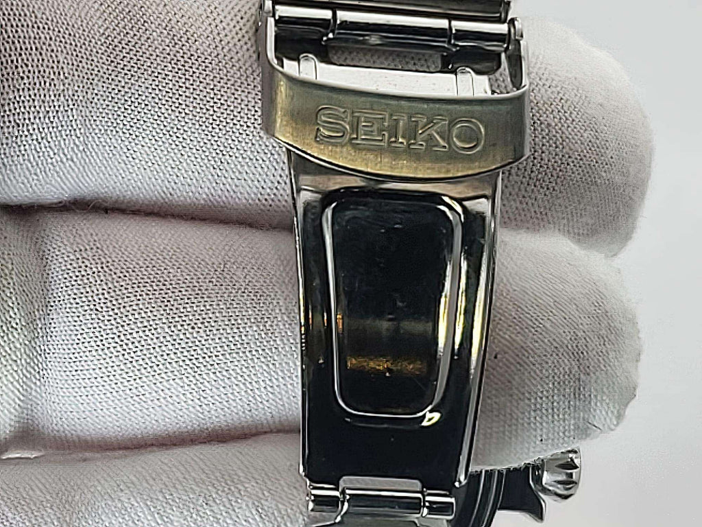 Close-up of a Seiko Flightmaster stainless steel watch clasp held against a white textured fabric background.