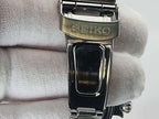 Close-up of a Seiko Flightmaster stainless steel watch clasp held against a white textured fabric background.