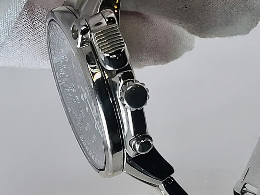 Close-up side view of a stainless steel Seiko Flightmaster wristwatch with a silver case, black crown and pushers, and a white dial, held by a white-gloved hand against a light gray background.