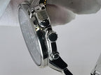 Close-up side view of a stainless steel Seiko Flightmaster wristwatch with a silver case, black crown and pushers, and a white dial, held by a white-gloved hand against a light gray background.