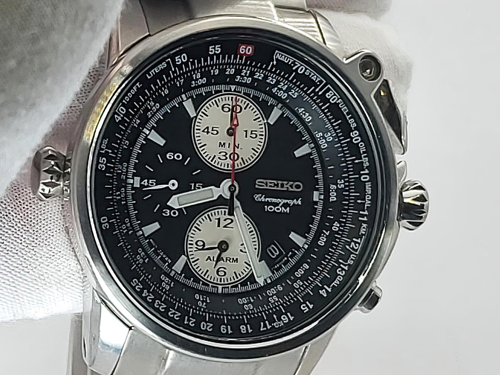 A Seiko Flightmaster chronograph watch with a black dial, silver stainless steel case, and white strap, shown close-up against a light background.