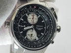A Seiko Flightmaster chronograph watch with a black dial, silver stainless steel case, and white strap, shown close-up against a light background.