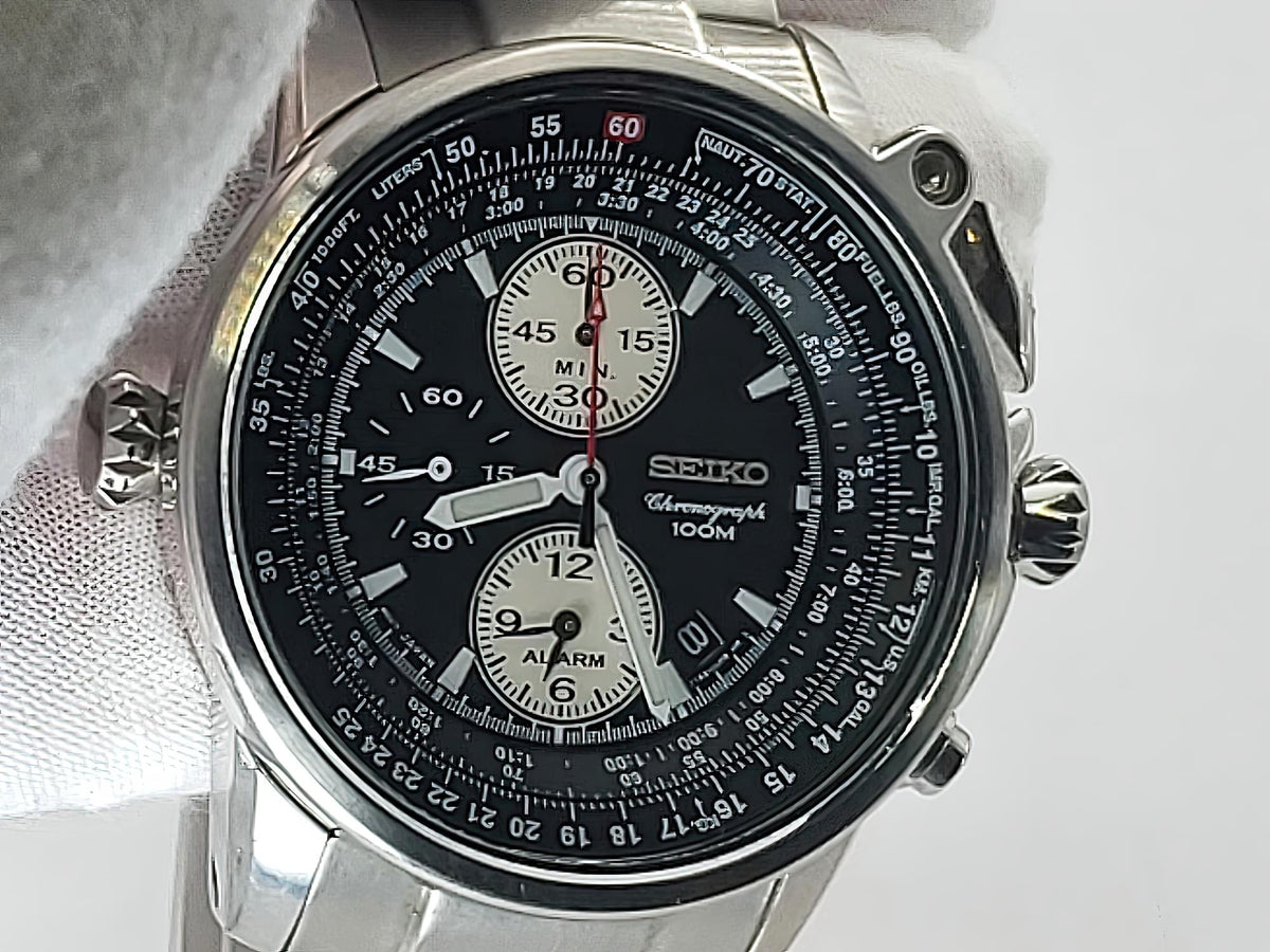 A Seiko Flightmaster chronograph watch with a black dial, silver stainless steel case, and white strap, shown close-up against a light background.