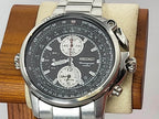 A Seiko Flightmaster chronograph watch with a silver stainless steel case and link bracelet, featuring a black dial with white subdials and white hour markers, displayed on a beige cushion inside a wooden box.