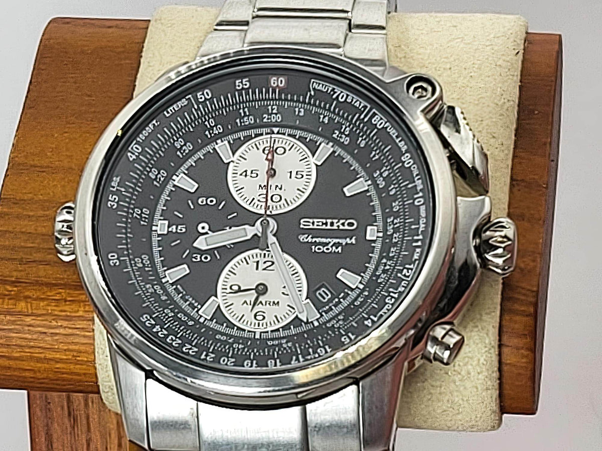 A Seiko Flightmaster chronograph watch with a silver stainless steel case and link bracelet, featuring a black dial with white subdials and white hour markers, displayed on a beige cushion inside a wooden box.