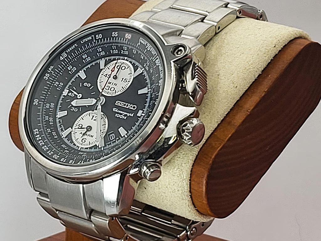 A Seiko Flightmaster stainless steel chronograph watch with a black dial and silver case, displayed on a wooden stand with a cream-colored velvet cushion.