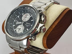 A Seiko Flightmaster stainless steel chronograph watch with a black dial and silver case, displayed on a wooden stand with a cream-colored velvet cushion.