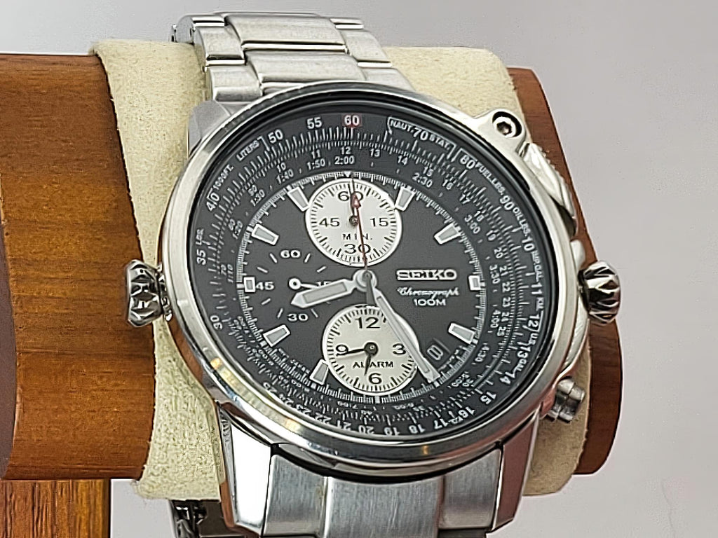 A Seiko Flightmaster stainless steel chronograph watch with a dark gray dial and silver-tone metal bracelet, displayed on a beige cushion mounted on a wooden stand.