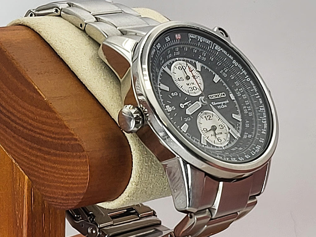 A Seiko Flightmaster stainless steel chronograph watch with a dark gray dial and silver-tone metal bracelet, displayed on a beige velvet cushion mounted on a wooden stand against a light gray background.