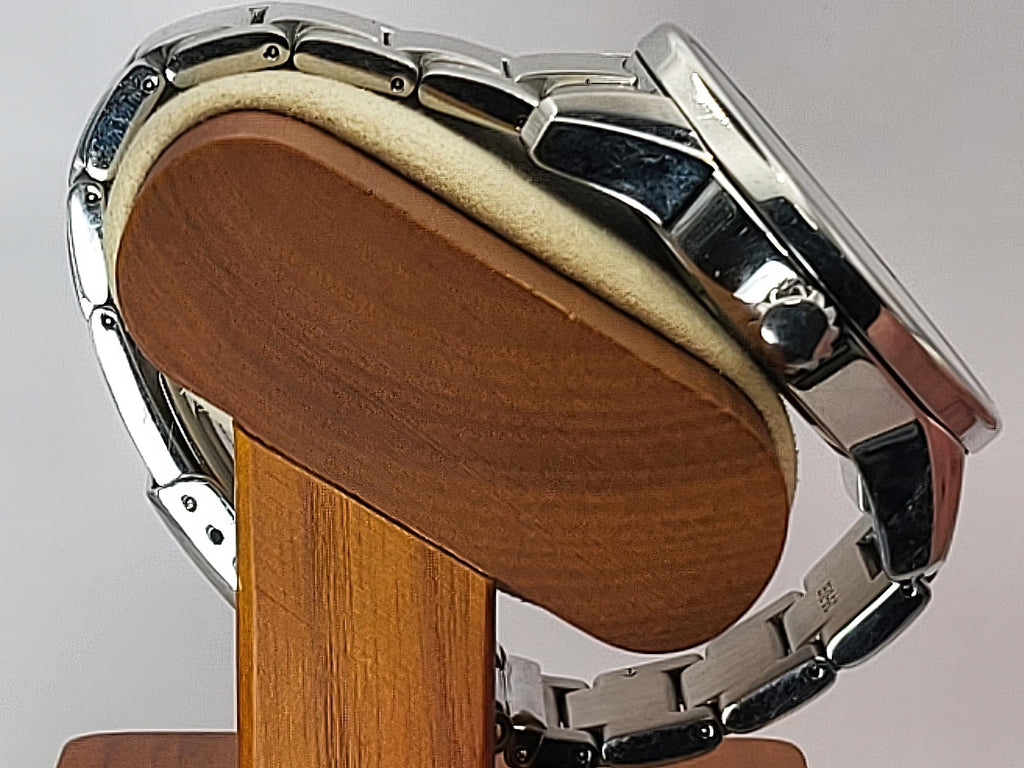 A close-up of a silver stainless steel Seiko Flightmaster watch with a metal link bracelet, resting on a wooden display stand with a beige cushion.