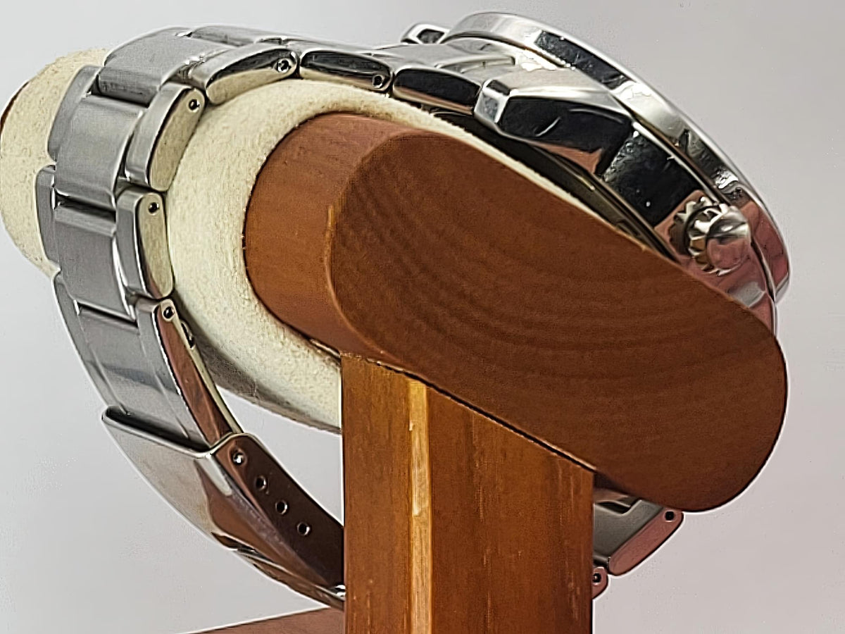 A close-up of a silver stainless steel Seiko Flightmaster watch with a metal link bracelet, displayed on a wooden stand with a cream-colored felt cushion against a light gray background.