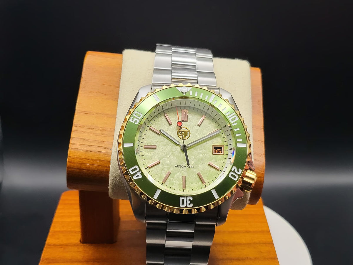 The Coconut SJT Original wristwatch with a green bezel and light green dial, displayed on a wooden stand against a dark background.