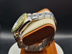 The Coconut SJT Original wristwatch with a green dial, displayed on a wooden stand with a cream cushion against a dark background.