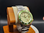 The Coconut SJT Original wristwatch with a green bezel and light green dial, displayed on a wooden stand against a dark background.