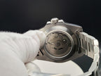 Close-up of The Memo SJT Original wristwatch with its back open, showing the mechanical movement, held by a white-gloved hand against a dark background.