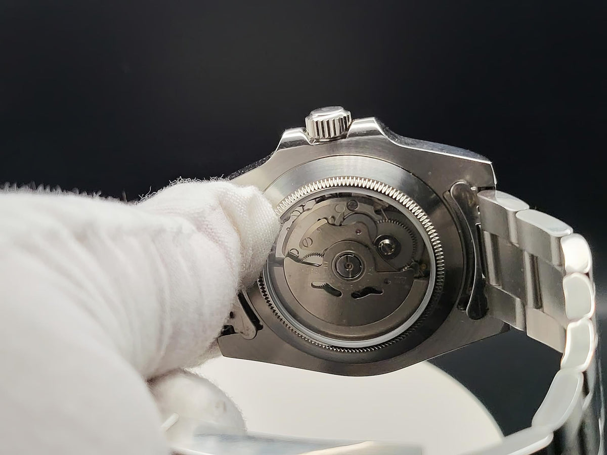 Close-up of The Memo SJT Original wristwatch with its back open, showing the mechanical movement, held by a white-gloved hand against a dark background.