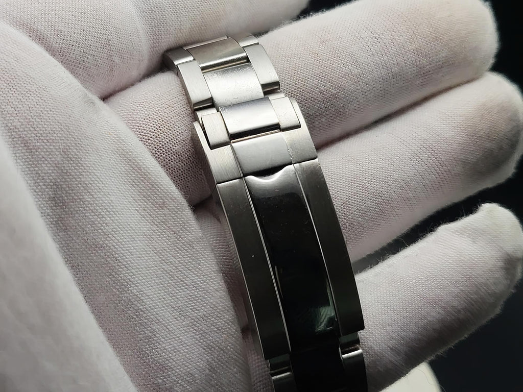 A close-up of a polished stainless steel link bracelet for The Memo SJT Original wristwatch held in a white-gloved hand against a dark background.